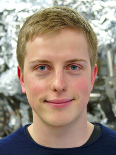 Philipp Kagerer mit kurzem Haar vor metallisch glänzendem Hintergrund.